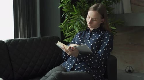 Young Woman Reading Storybook on Couch at Home