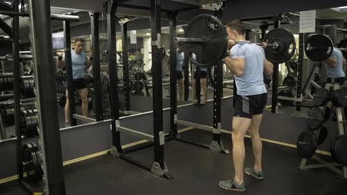 Attractive man holding barbell behind neck at the gym.