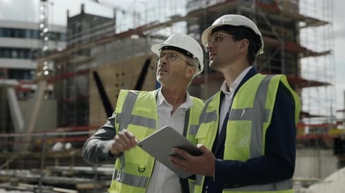 Männer mit Schutzhelmen nutzen Tablet auf der Baustelle