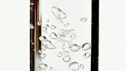 Makroaufnahme von klarem Wasser, das durch Gießen von Wasser in eine klare Pipette auf weißem Hintergrund sprudelt