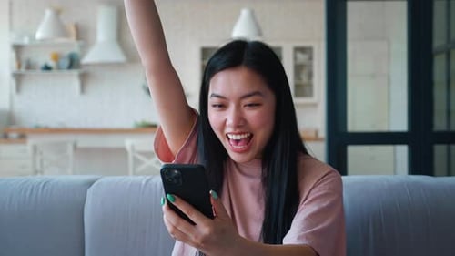 Excited woman looks at phone at home