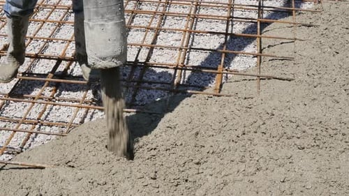 Ein männlicher Baumeister leitet den Fluss der Betonmischung aus einem dicken Schlauch einer Betonpumpe, während er eine