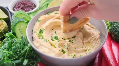 Dipping Flatbread into Creamy Hummus with Vegetables