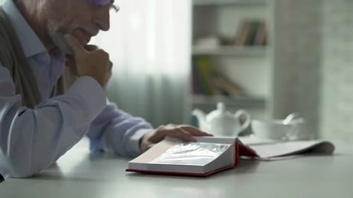 Hombre mayor mirando fotos en álbum de fotos y cerrándolo, recuerdos felices