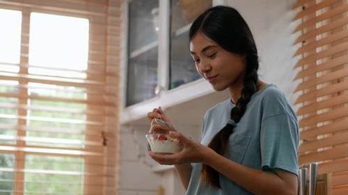 Woman Eating Yogurt with Fruit in Kitchen