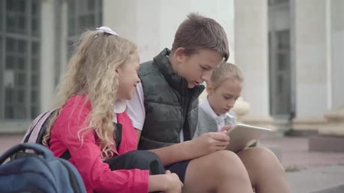 Positive Caucasian Schoolboy Resting with Classmates on School Stairs. Side View of Carefree Boy and
