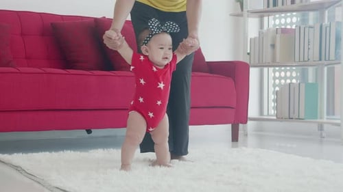 Happy family with mother support baby step walk in the living room at home.