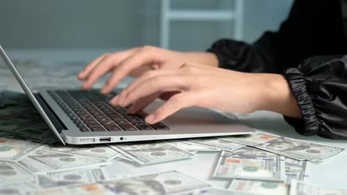 Hands Typing on Laptop Surrounded by Money
