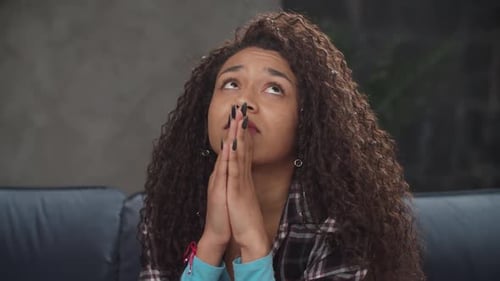 Pensive Woman Praying with Clasped Hands Indoors
