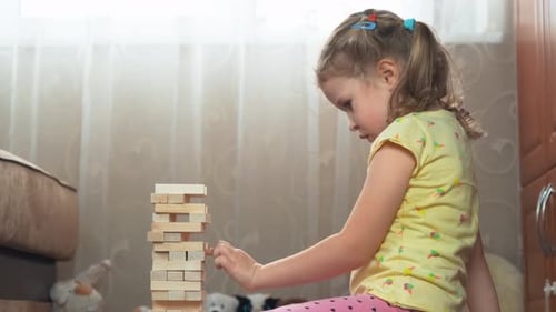 Lockiges, blondes vierjähriges Mädchen spielt Jenga-Spiel
