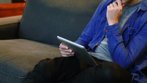 Young Adult Uses Tablet on Sofa