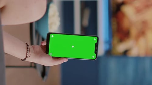 Closeup of Young Woman Holding Vertical Smartphone with Green Screen Watching Social Media Content