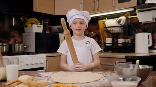 Portrait of a Cute Boy in a White Apron and a Chef's Hat with a Rolling Pin