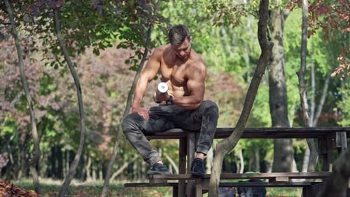 Sportsman training shoulder muscles in nature. Muscular athlete sitting in the park and pumping his