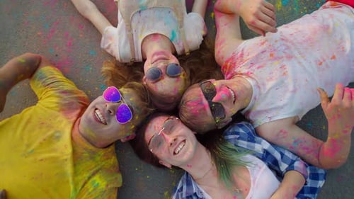 A Multi-ethnic Group of Friends, Smeared with Holi Powder, Lies on the Pavement, Laughing, Looking
