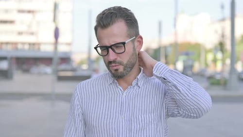 Man Rubs Sore Neck in Urban Setting