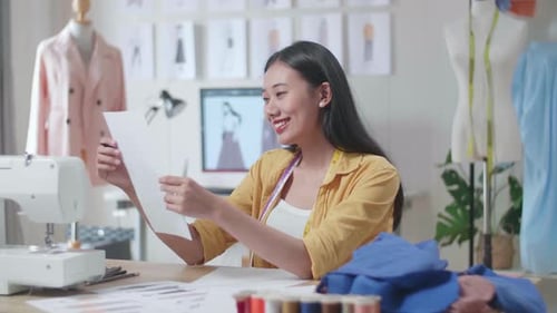 Female Designer With Sewing Machine Designing Clothes On Paper Before Looking It In The Studio
