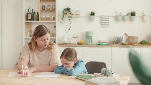 Woman Helping Young Girl With Homework In Kitchen