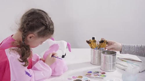 Little girl painting paper mache figurines with acrylic paint for her homeschooling art project.