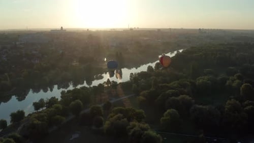 Beautiful flight at the sunrise of a red balloon over a river, forest, green trees.