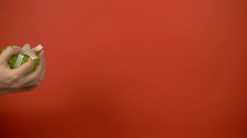 Hands Unwrap Green Gift on Red Background