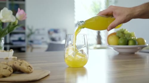 Refreshing Yellow Juice Pouring into Glass with Ice