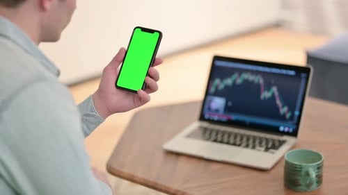 Person Tapping Green Screen Phone Next to Laptop