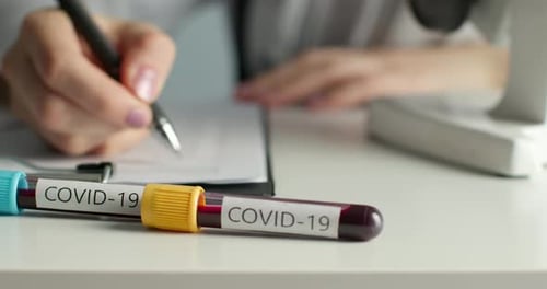 Close-up Shot. The Doctor Is Filling Out the Documents. In the Foreground Are Test Tubes with COVID