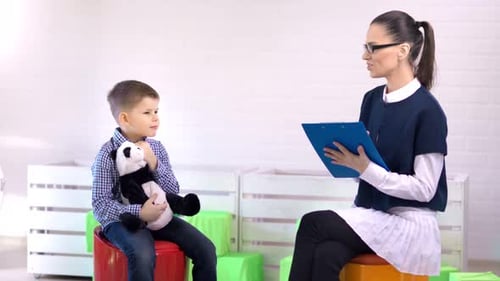 Smiling Female Professional Child Psychologist Talking with Little Boy Medium Long Shot