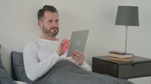 Man Using Tablet Device Lying in Bed at Home