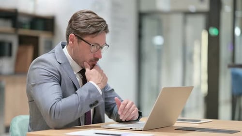 Pensive Businessman Thinking and Working on Laptop in Office
