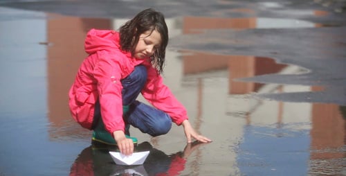 Girl Plays with Paper Boat in City Puddle