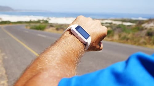 Man Taps Smartwatch while Running on Beach Road