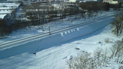 Flug über die Eisenbahn. Ein Zug fährt entlang der Schienen. Winterliche Industrielandschaft.