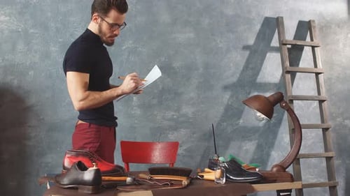 Man at Table Writing in Shoe Maker's Workshop