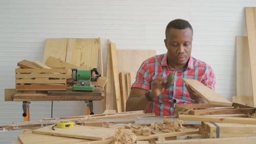Carpenter african american man looking and using sandpaper to rub wooden plank at workshop
