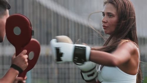 Boxing Training Young Woman with Long Hair Punching the Mitts on the Hands of Her Male Trainer
