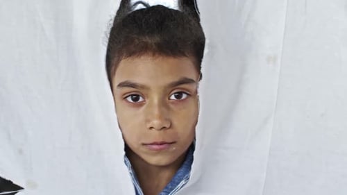 Jeune fille réfugiée debout derrière un tissu déchiré