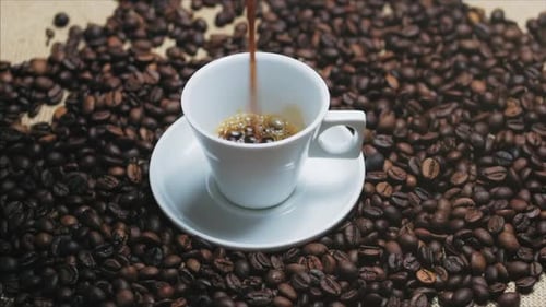 Pouring Hot Coffee into White Cup Surrounded by Beans