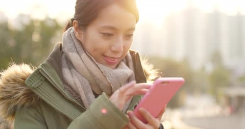 Woman Using Pink Phone in City at Sunset