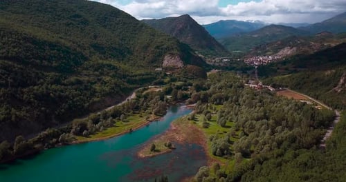 Aerial horizontal 4K footage of a lake in a green natural environment with mountains and a village.