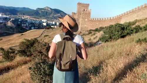 Active Travel Backpacker Woman Walking on Hilly Terrain Near Medieval Antique Wall Back View