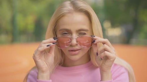 Close-up Face of Beautiful Blond Woman Putting Down Sunglasses and Winking at Camera. Portrait of