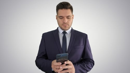Serious businessman texting message on his phone on gradient