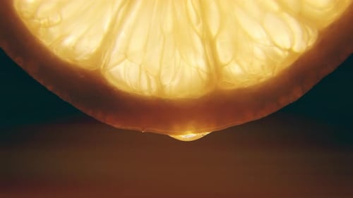 Une photo macro d'une goutte de jus d'orange coulant sur une tranche d'orange crue fraîche rétroéclairée sur un fond noir