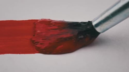 Pinsel mit roter Farbe zeichnet im Makro eine Linie auf weißem Papier