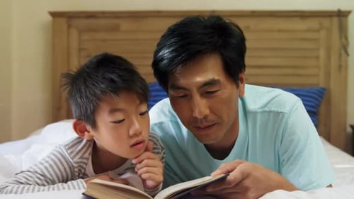 Father and Son Reading a Book Together in Bed