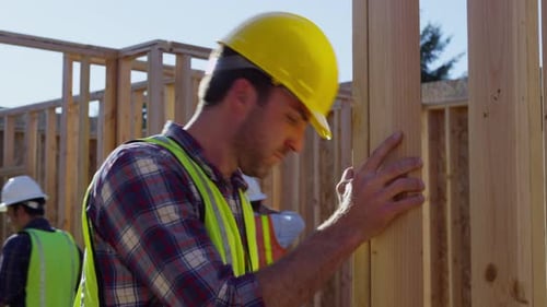 Construction Worker Hammers Lumber at Building Site