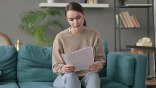 Woman Reading Paperwork on Sofa Indoors