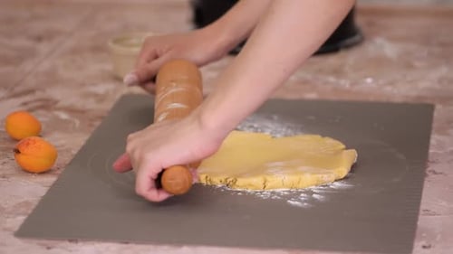 Close up of woman rolling dough with rolling pin on kitchen table.